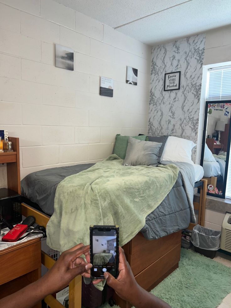 a person holding up a camera in front of a bed with a green blanket on it