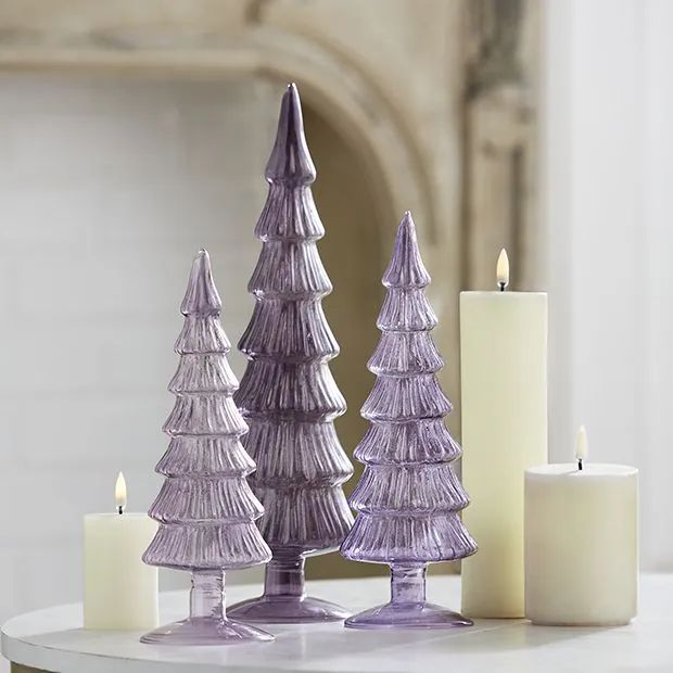 three purple christmas trees sitting on top of a white table next to candles and a fireplace