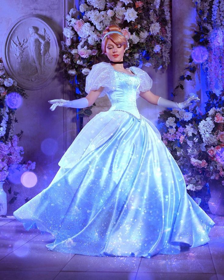 a woman in a blue dress and white gloves is standing on stage with flowers behind her