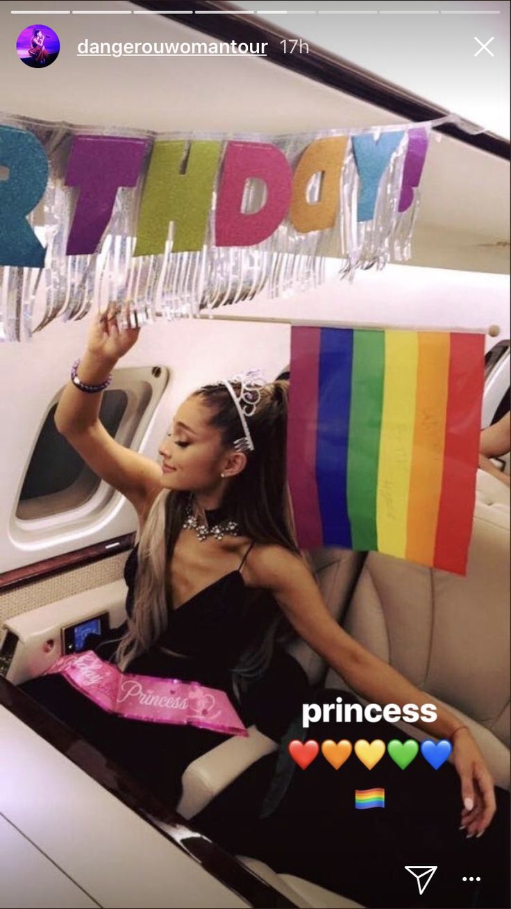 a woman sitting in the back of a car holding a rainbow flag