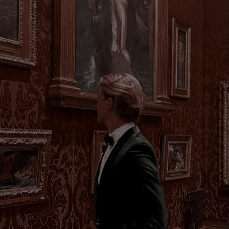 a man in a tuxedo is looking at paintings on the wall behind him