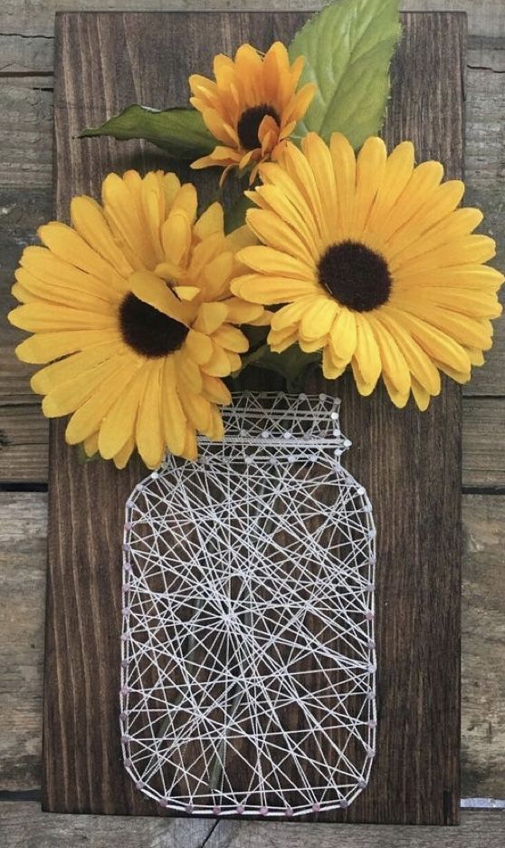 some yellow sunflowers are in a mason jar on a wooden board with string