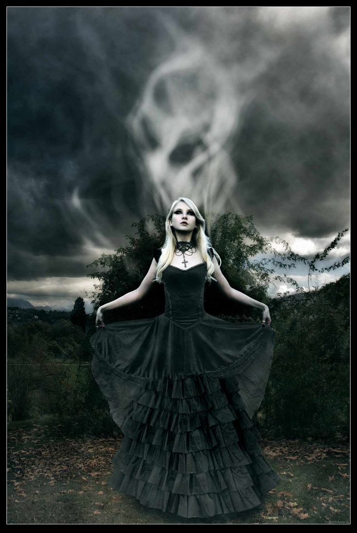 a woman in a long black dress with a skull on the back and clouds behind her