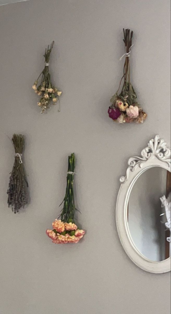 flowers are hanging on the wall next to a mirror and vases with dried flowers