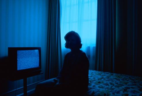 a person sitting on a bed in front of a flat screen tv with blue light coming from the window