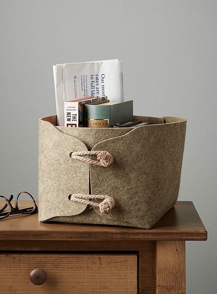 a wooden table topped with a brown basket filled with books and other items next to a pair of glasses