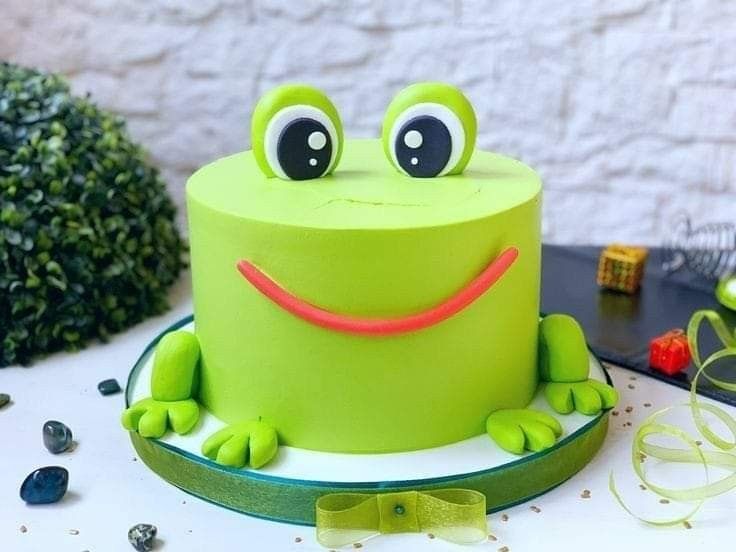 there is a green cake with a frog face on it's head and eyes