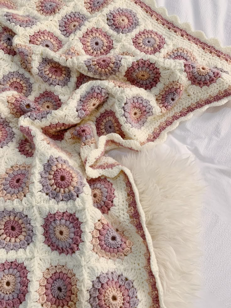 a crocheted blanket is laying on top of a white bed with fluffy pillows