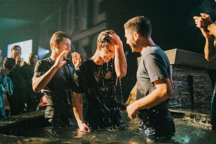 three men are standing in the water and one is covering his eyes with his hands