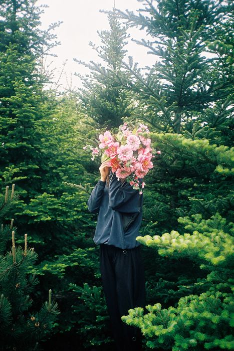 a person standing in front of some trees with flowers on their head and looking up at the sky