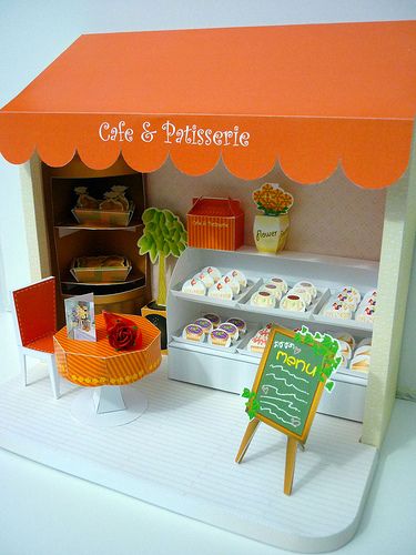 an orange and white display case with cupcakes on it's sides, next to a sign that says cafe & patissee