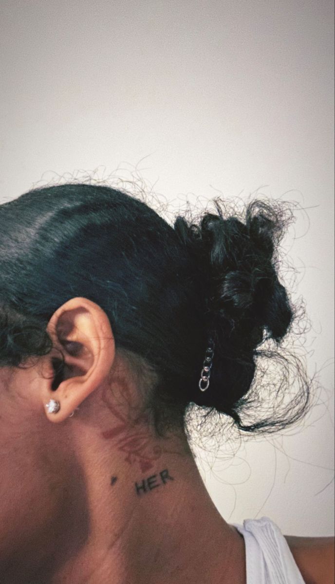 a woman with a tattoo on her neck and behind her ear is looking at the camera