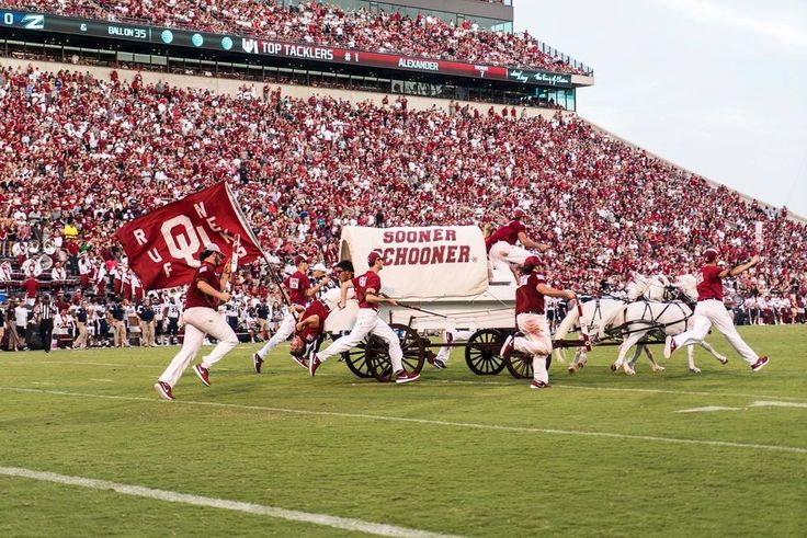 a group of men riding on the back of horses pulling a wagon down a field