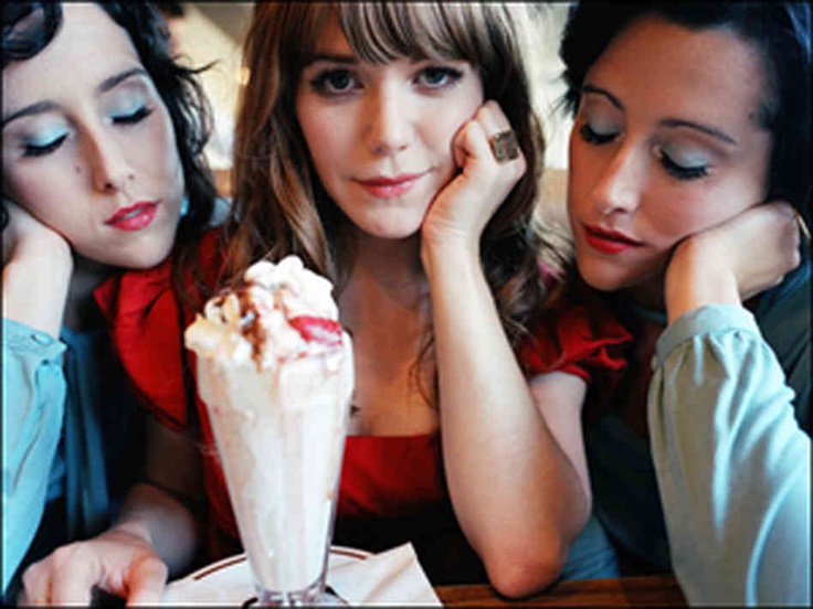 three young women sitting at a table with an ice cream sundae in front of them