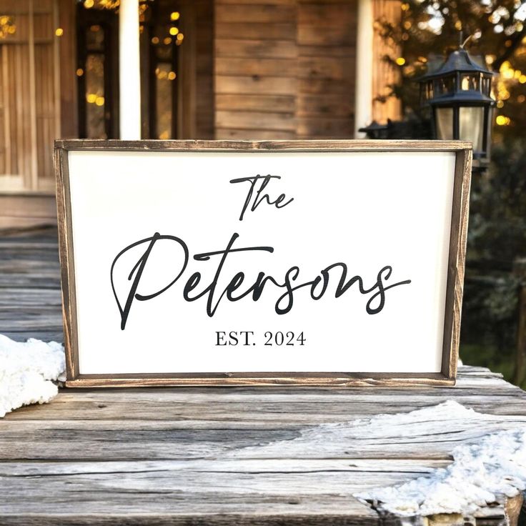 a sign sitting on top of a wooden table in front of a house with snow