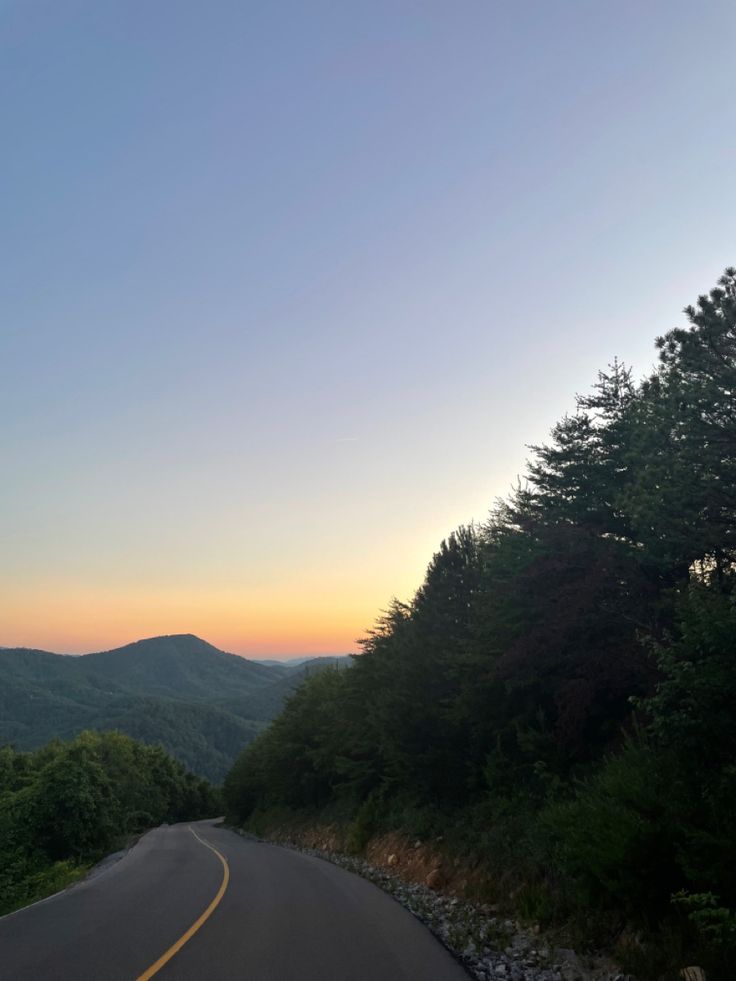 the sun is setting on a mountain road with trees and mountains in the back ground