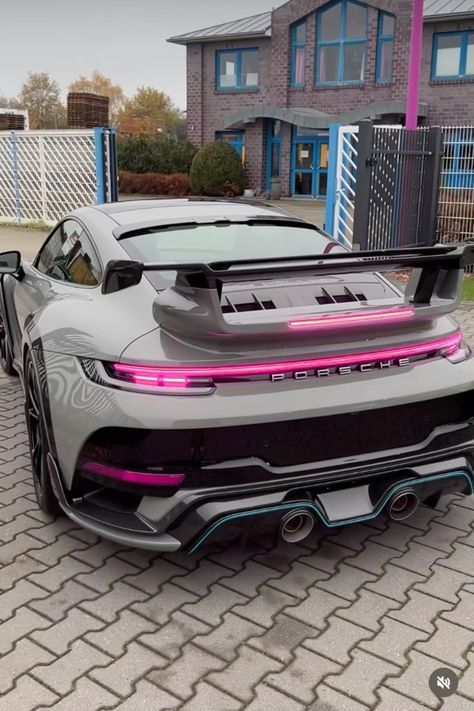 a grey sports car parked in front of a brick building with pink lights on it