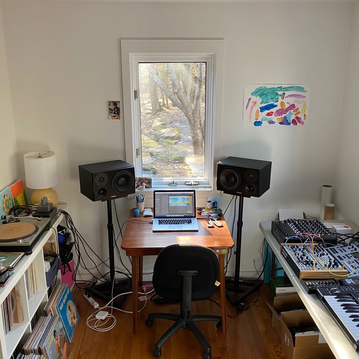 there is a desk with speakers and a laptop on it in front of a window