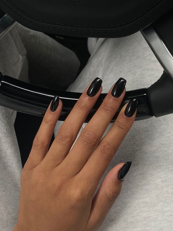 a woman's hand with black nail polish on her nails, sitting in a chair