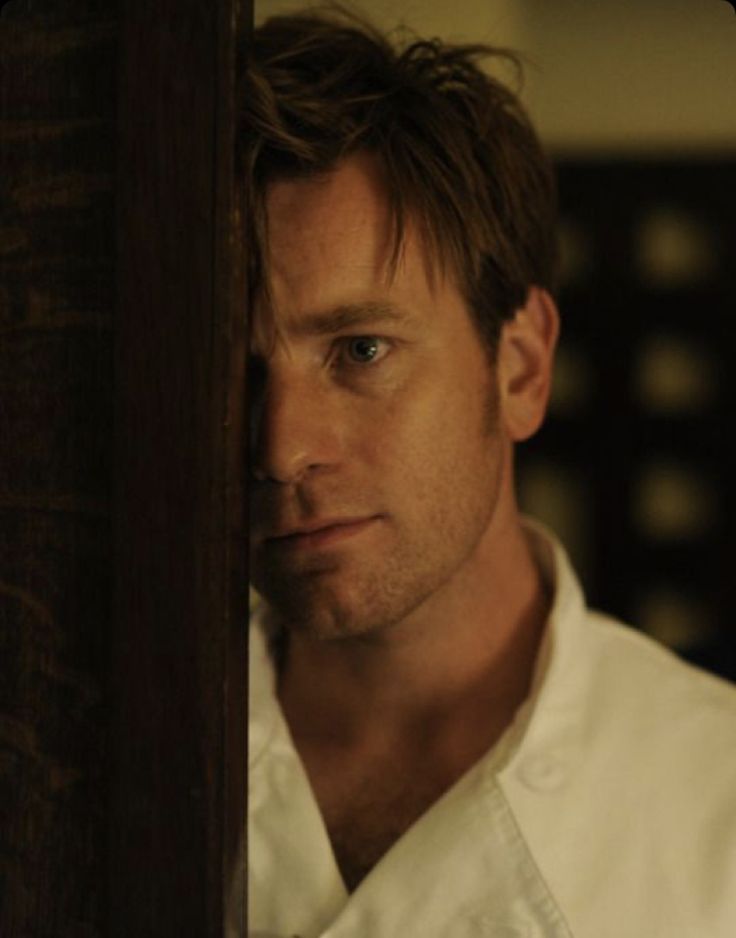 a man in a white shirt and tie looking out from behind a wooden paneled wall