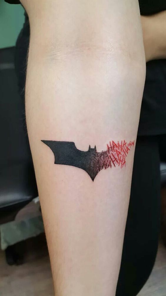 a tattoo on the leg of a woman with red writing and a black bat design