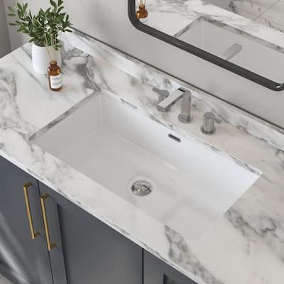 a bathroom sink with marble counter top and mirror in the backround, next to a plant