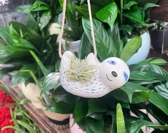 a ceramic bird ornament hanging from a rope in front of some potted plants