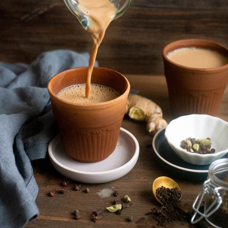 two cups of coffee being poured into one cup and another mug with tea on the other