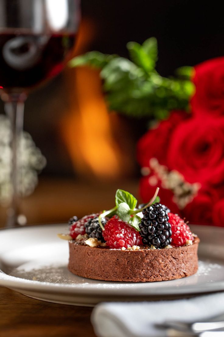 a chocolate cake with berries and whipped cream sits on a plate next to a glass of red wine