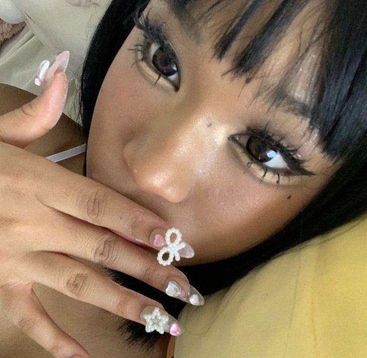 a woman with black hair and white nails holding her hand up to her face while looking at the camera