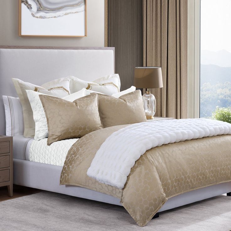 a bed with white and gold comforters in a bedroom next to a window overlooking the mountains