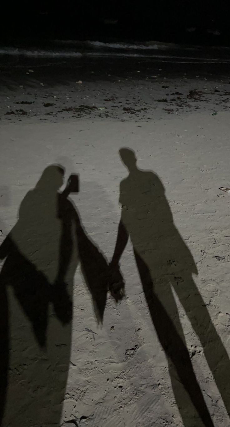 two people holding hands in the sand at night with their shadow cast on them,