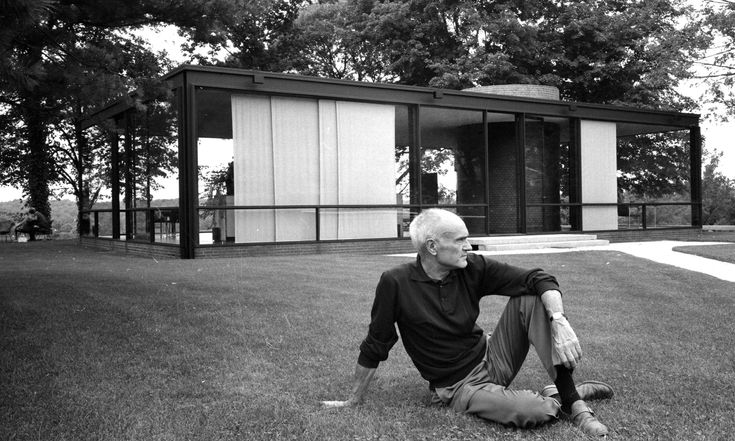 an older man sitting on the grass in front of a building with glass walls and doors