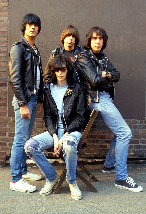 four young men sitting on a bench in front of a brick wall and wearing black leather jackets