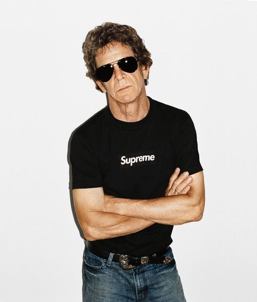 a man with his arms crossed standing in front of a white wall wearing sunglasses and a supreme t - shirt