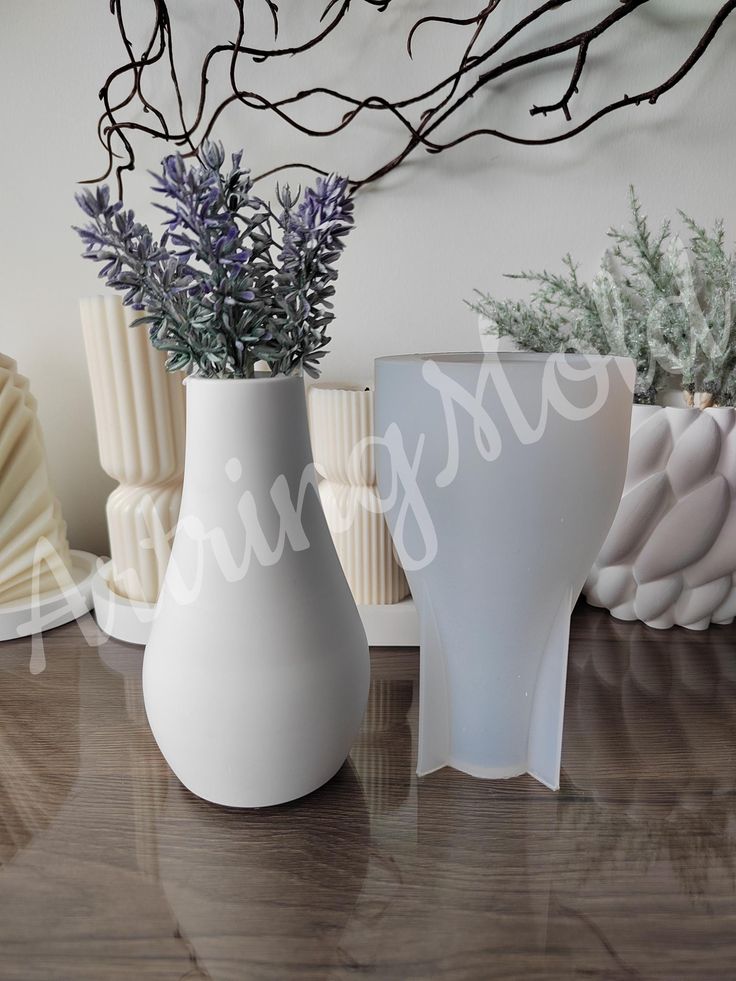 three white vases sitting on top of a wooden table next to plants and seashells