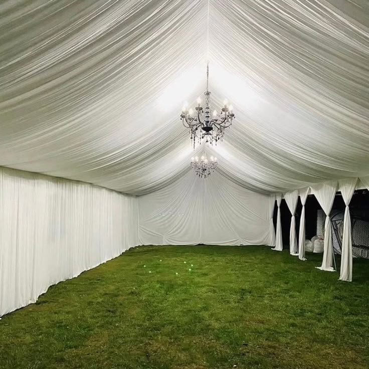 the inside of a tent with white drapes and chandelier