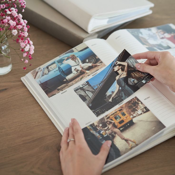 a person is holding an open book with photos on it and flowers in the background