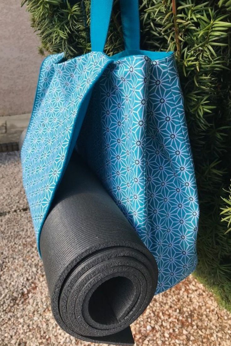 a blue bag hanging from the side of a tree with a black yoga mat in front of it