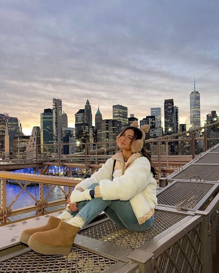 a woman sitting on top of a metal fence next to a cityscape at dusk