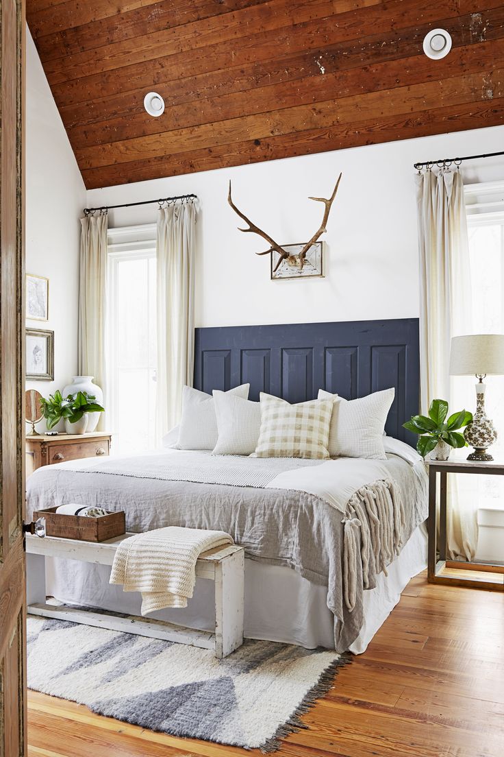 a bed sitting in a bedroom next to two windows and a wooden ceiling above it