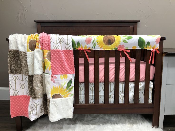 a baby crib with a sunflower quilt on it's cover and pink bedding