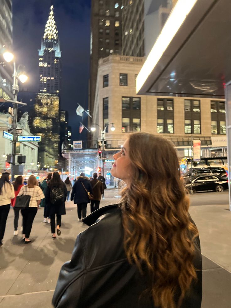 a woman standing in the middle of a city street at night with her head turned to the side