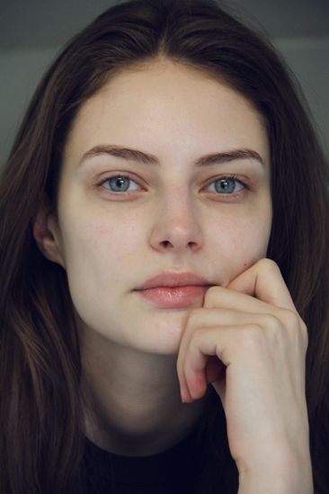 a woman with long brown hair and blue eyes is posing for the camera, her hand on her chin