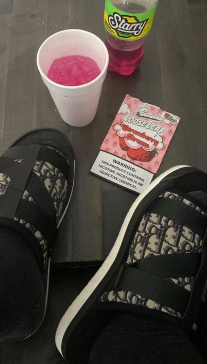 someone's feet with their shoes on, next to a cup of pink liquid