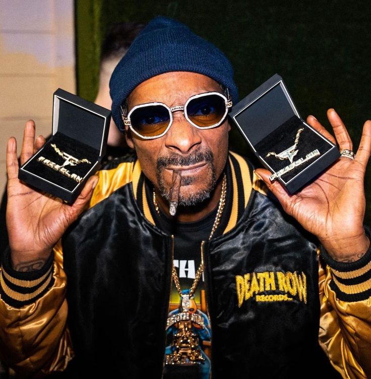 a man wearing sunglasses and a hat holding up two small boxes with rings on them