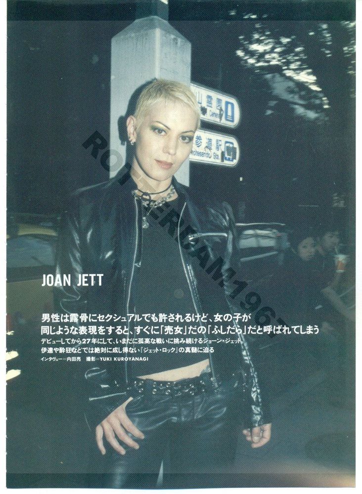 a woman in black leather jacket standing next to a street sign