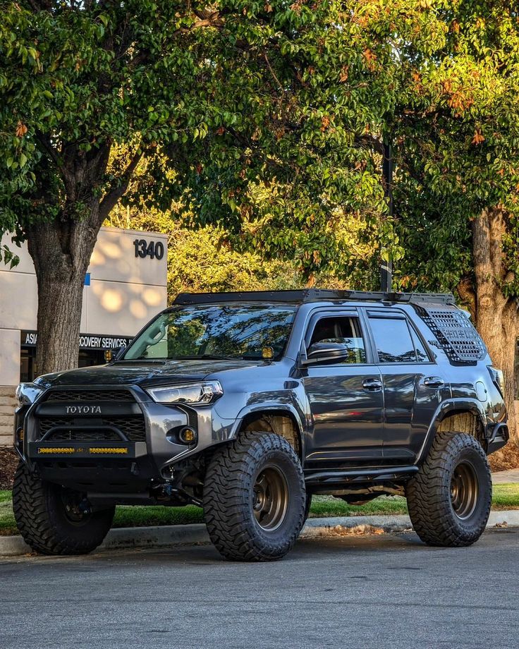 a large black truck parked on the side of a road next to trees and bushes