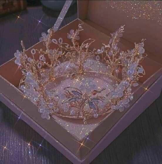 a tiara in a pink box on a wooden table with sparkles around it