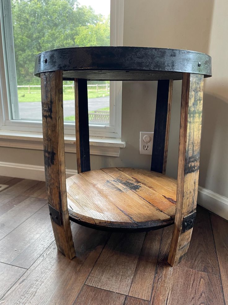 a round wooden table sitting on top of a hard wood floor next to a window